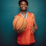 Happy male basketball player smiling while holding a ball in the studio.